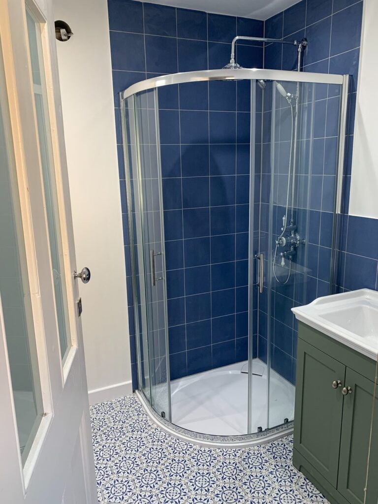 Blue tiled corner shower enclosure with patterned floor tiles and vanity unit installed in London bathroom.