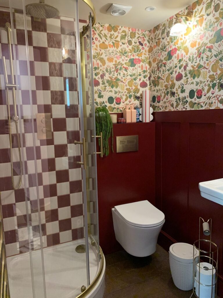 Modern bathroom with burgundy checkerboard shower tiles, floral wallpaper and concealed wall-hung toilet installed in London.