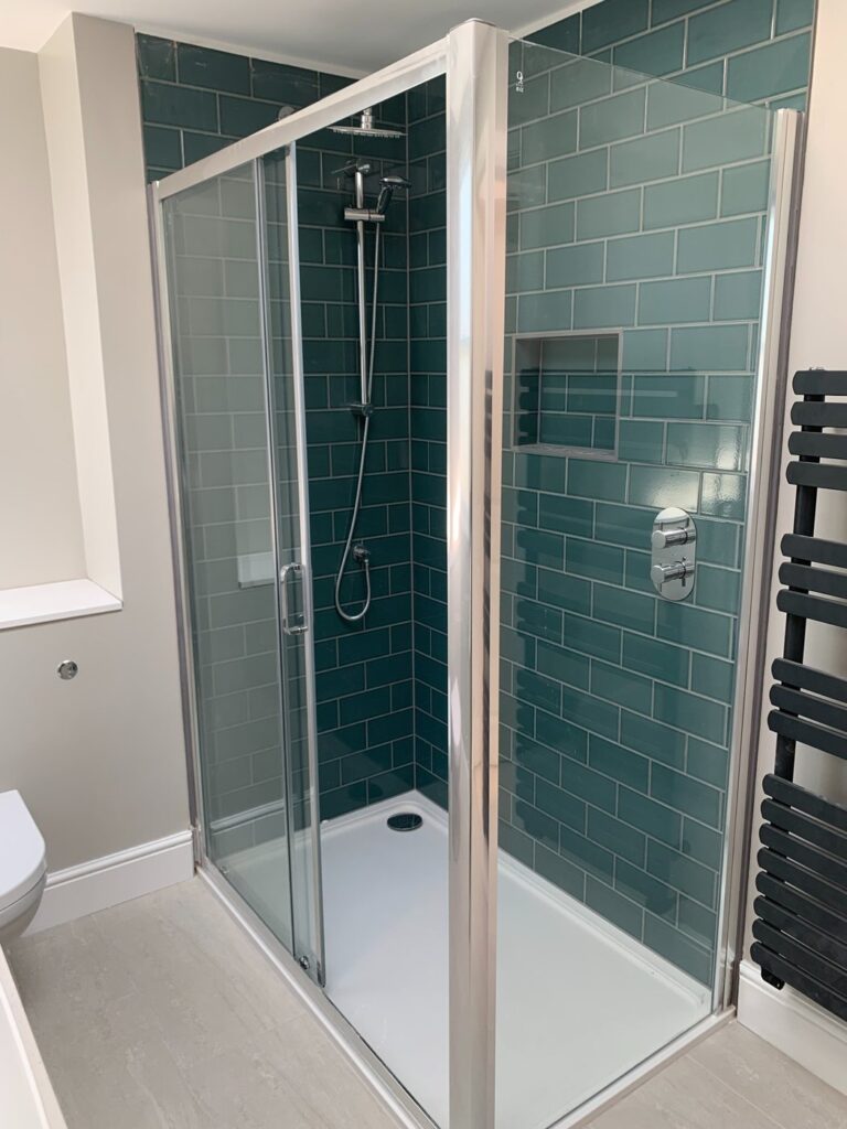 Modern shower enclosure with green subway tiles, recessed shower niche and chrome fittings installed in London bathroom