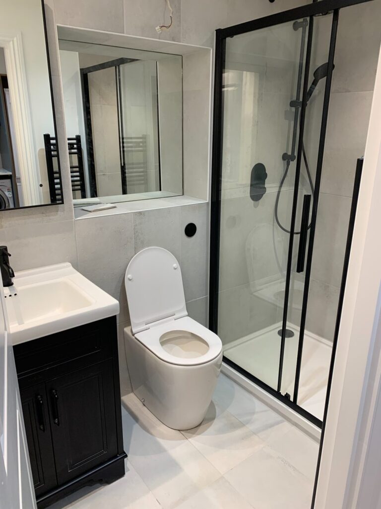 Modern bathroom with black framed shower enclosure, grey porcelain tiles and matte black vanity unit installed in London.
